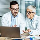 Praxisfinanzierung – junger Arzt und ältere Ärztin schauen auf Laptop