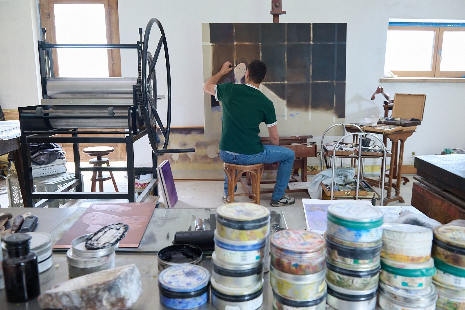 Djabril Boukehnaissi devant une de ses peintures à l'huile avec sa presse à gravure en arrière plan