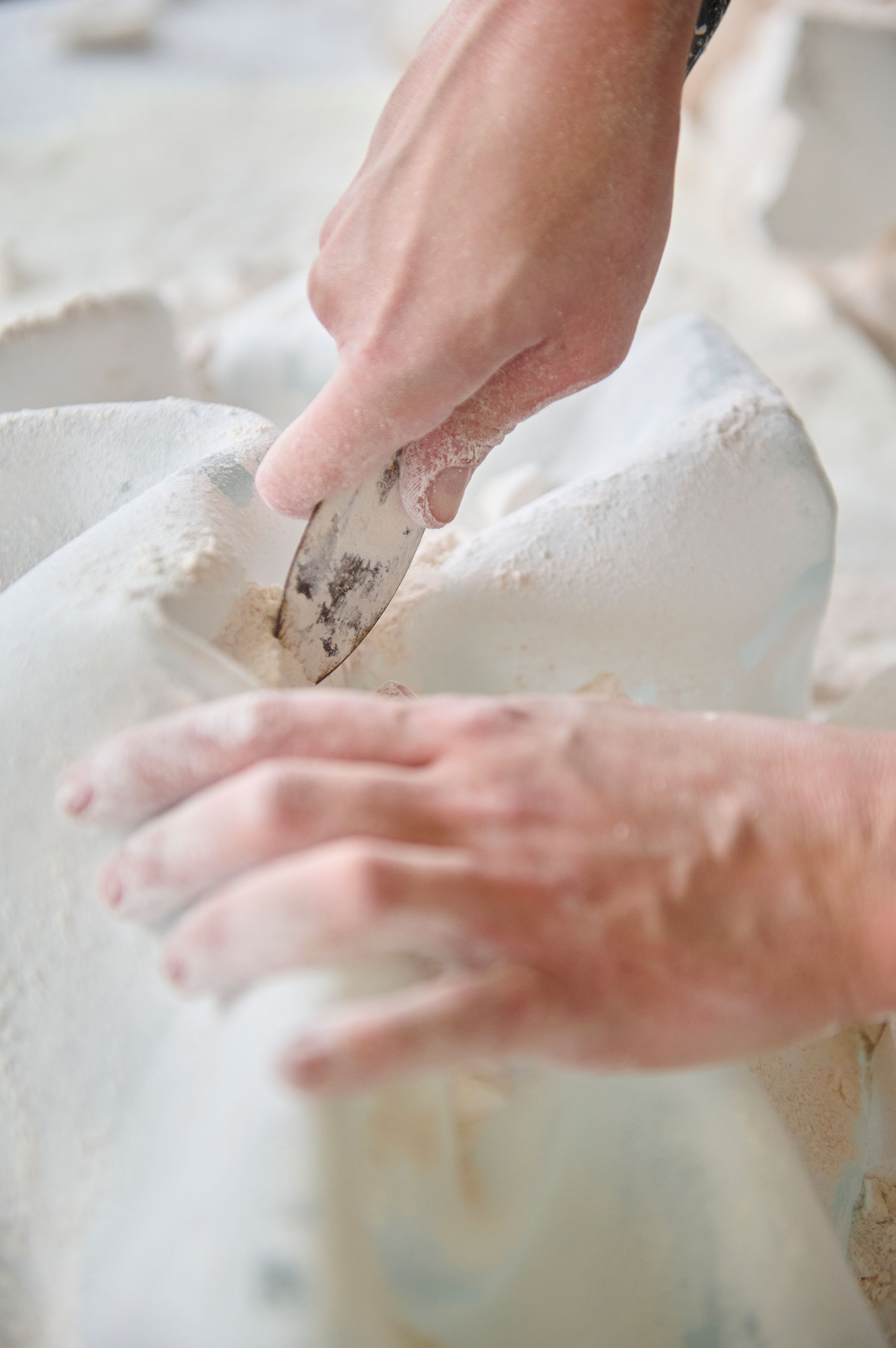 Reportage atelier Juliette Leperlier, gros plan des mains ôtant le plâtre du moule d'une sculpture en verre