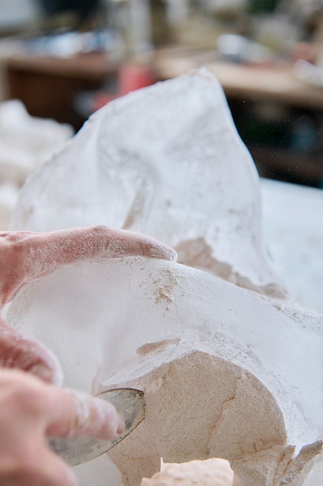 Main enlevant un bloc de plâtre d'une sculpture en verre