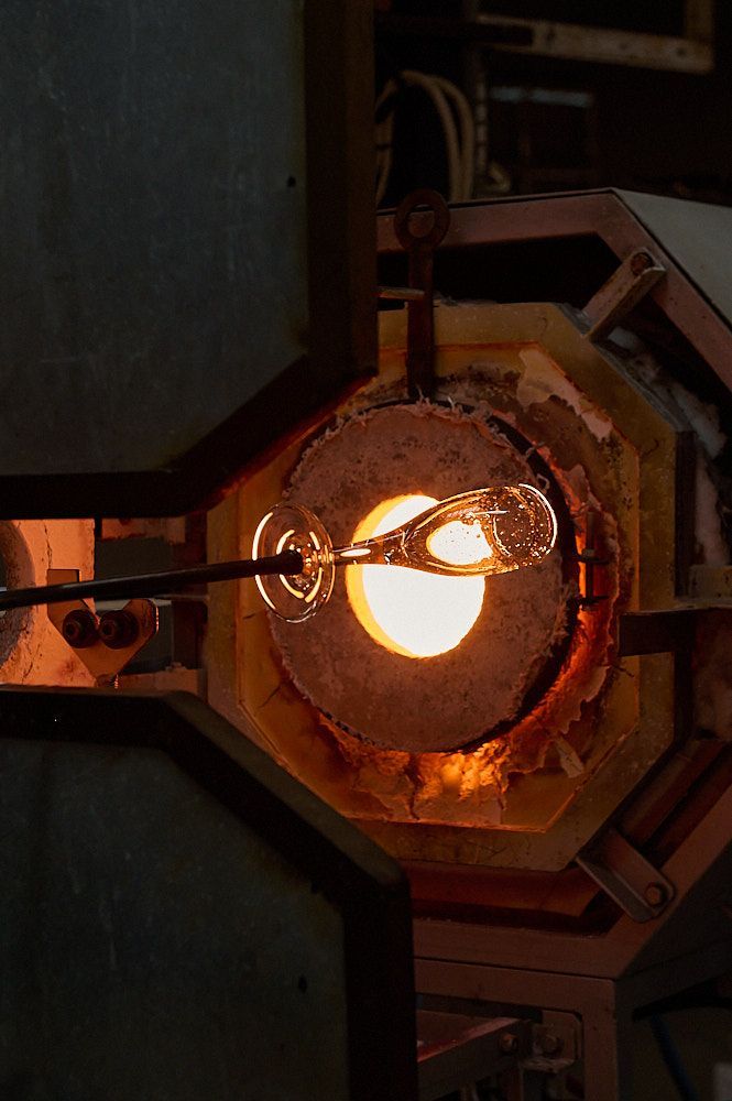 Verre à pied au bout d'une canne de soufflage devant le four