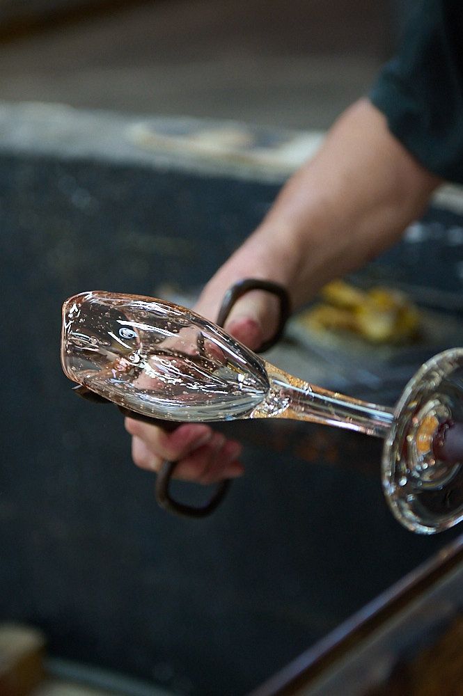Un souffleur de verre retire de la matière avec des ciseaux