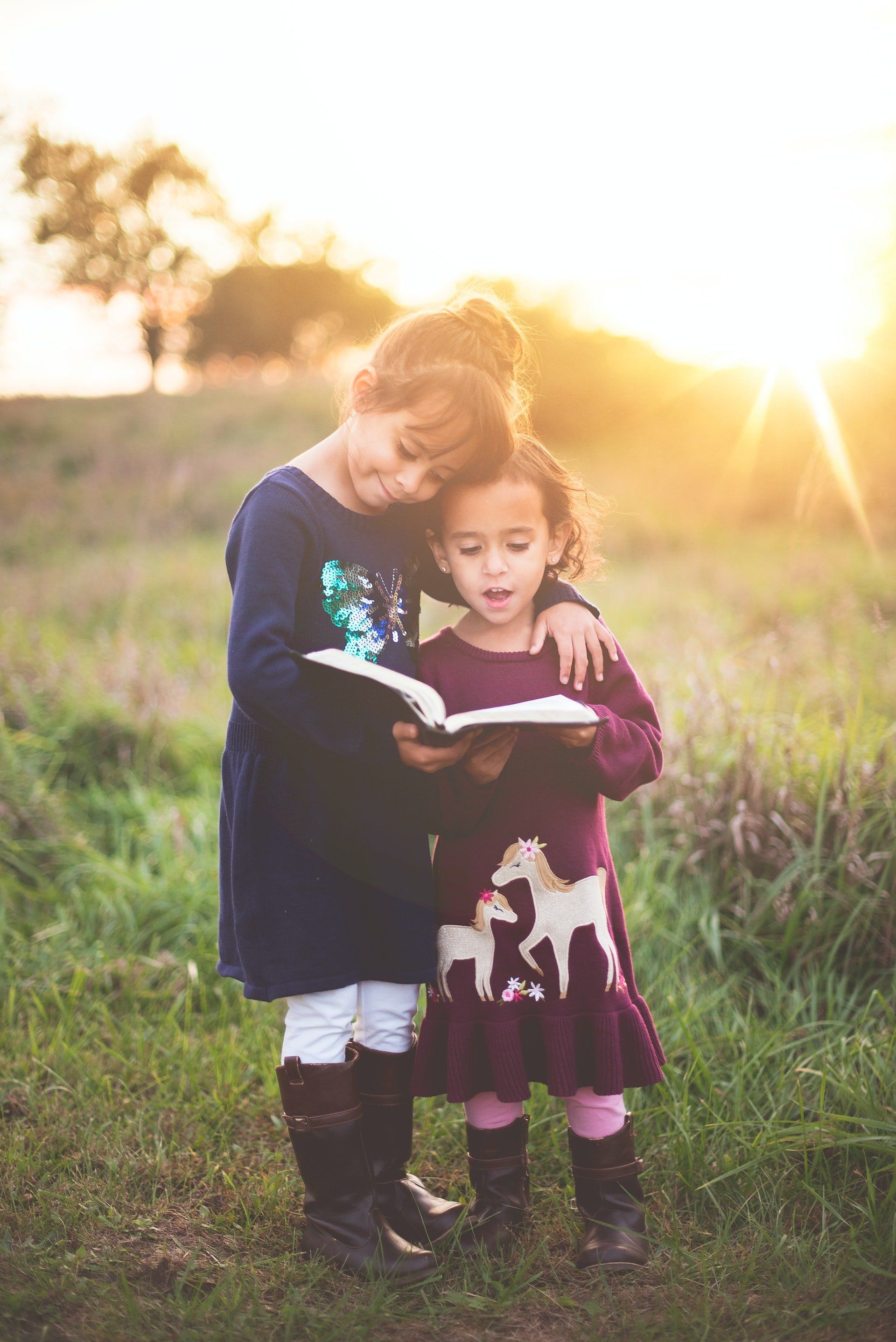 Image of two girls in a field holding a book. One appears to be reading or singing.