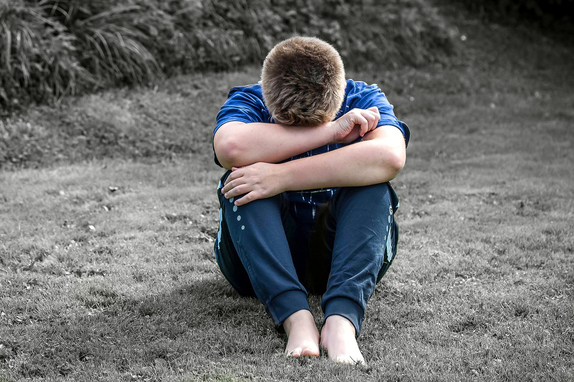 Image of a teenage boy sitting curled up on the ground.