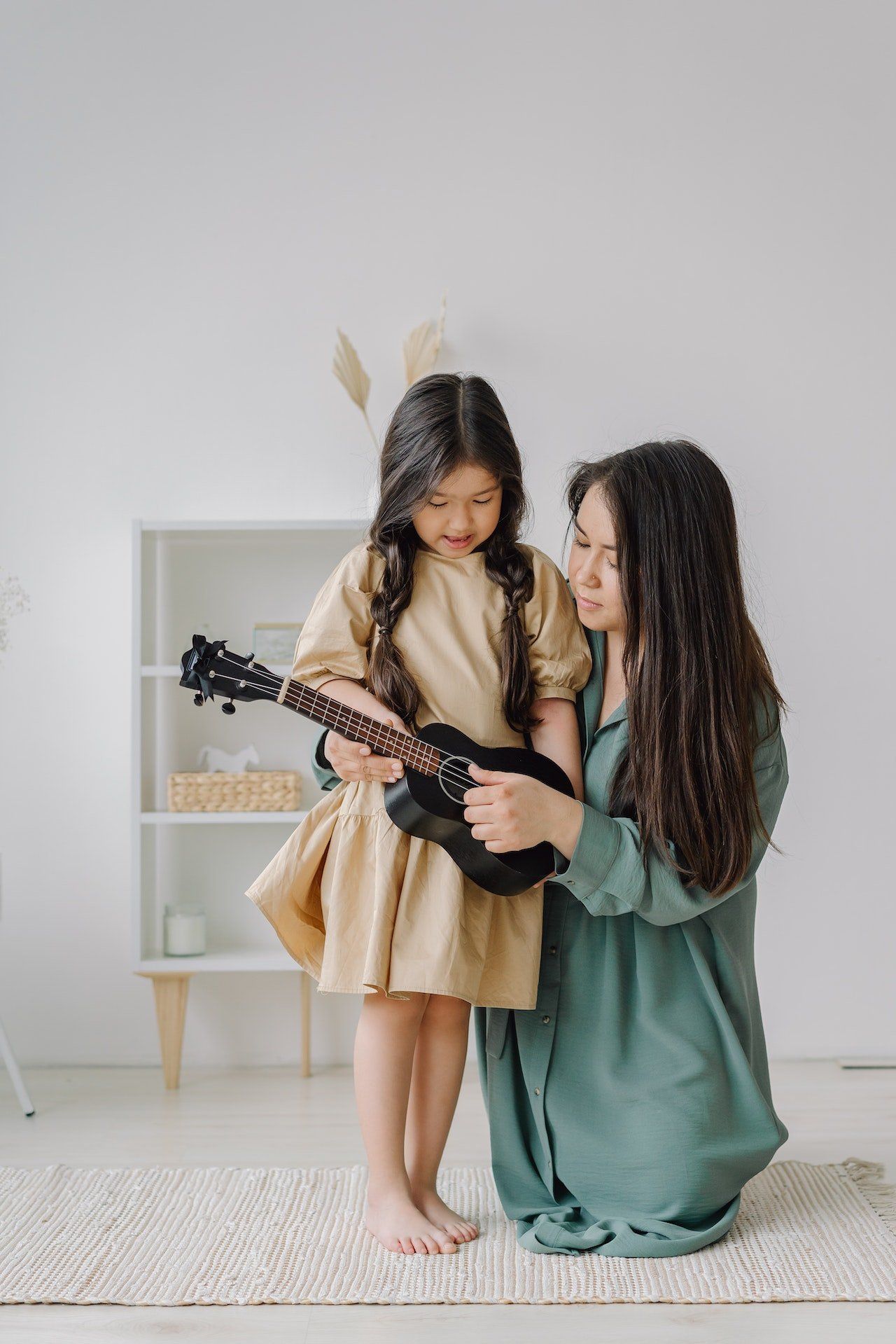 Image of a woman helping a young girl play a ukulele.