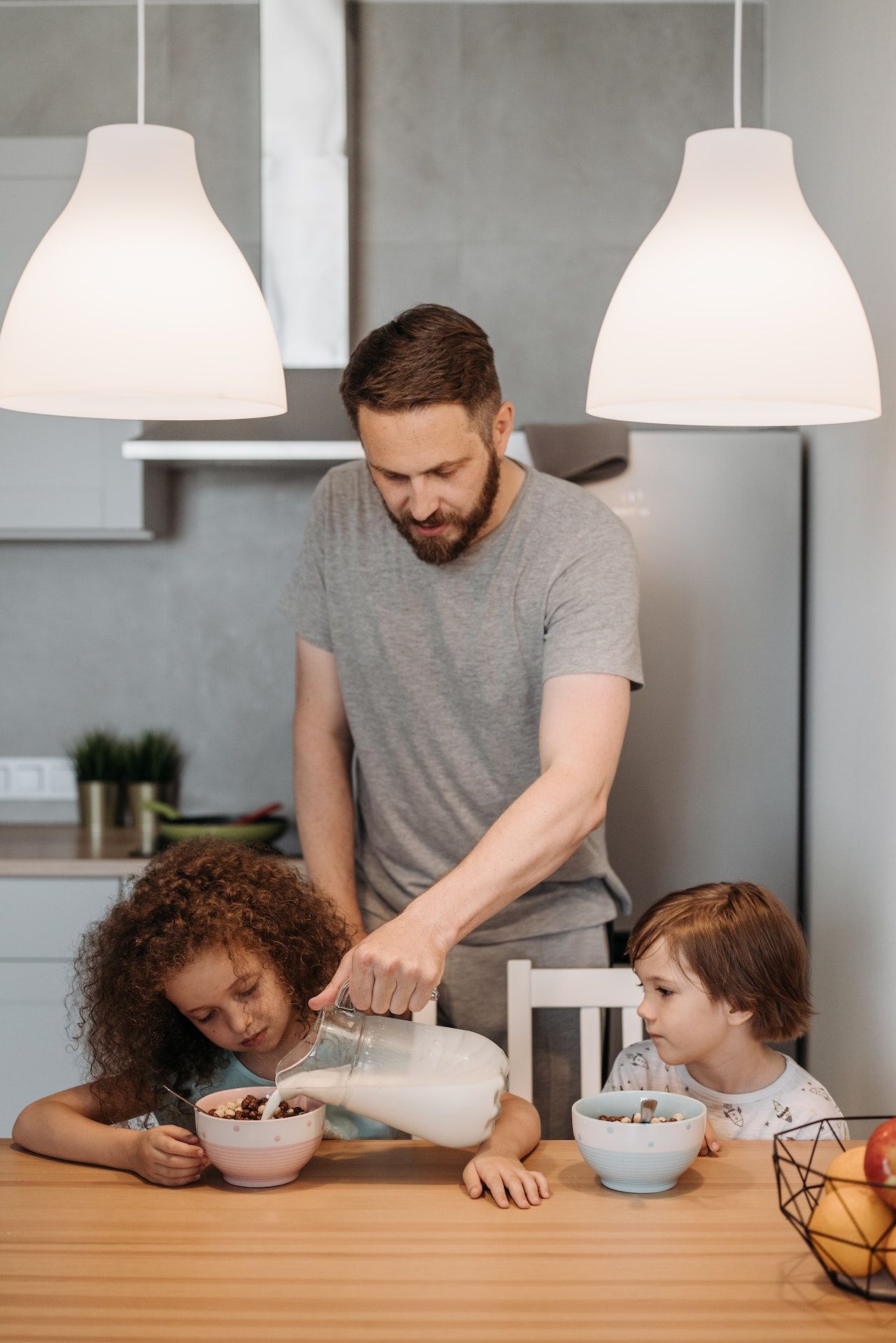 Image of a man pouring milk into a girl's cereal bowl.
