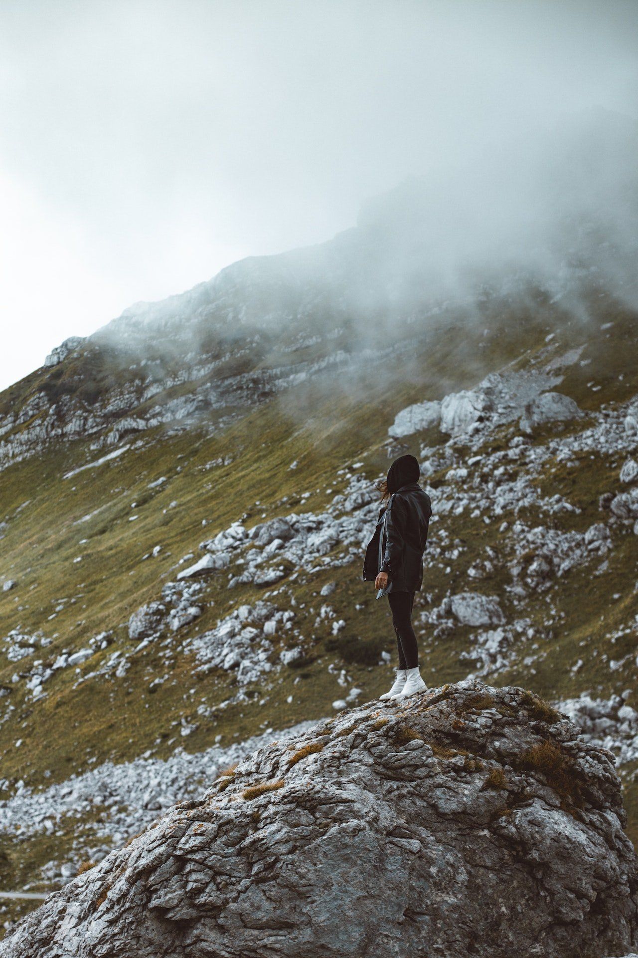 Image of a woman standing on a boulder on the side of a mountain.