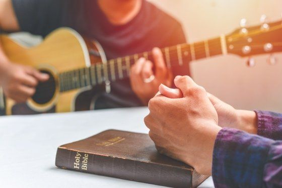 a person playing the guitar and another person resting their hands on the bible