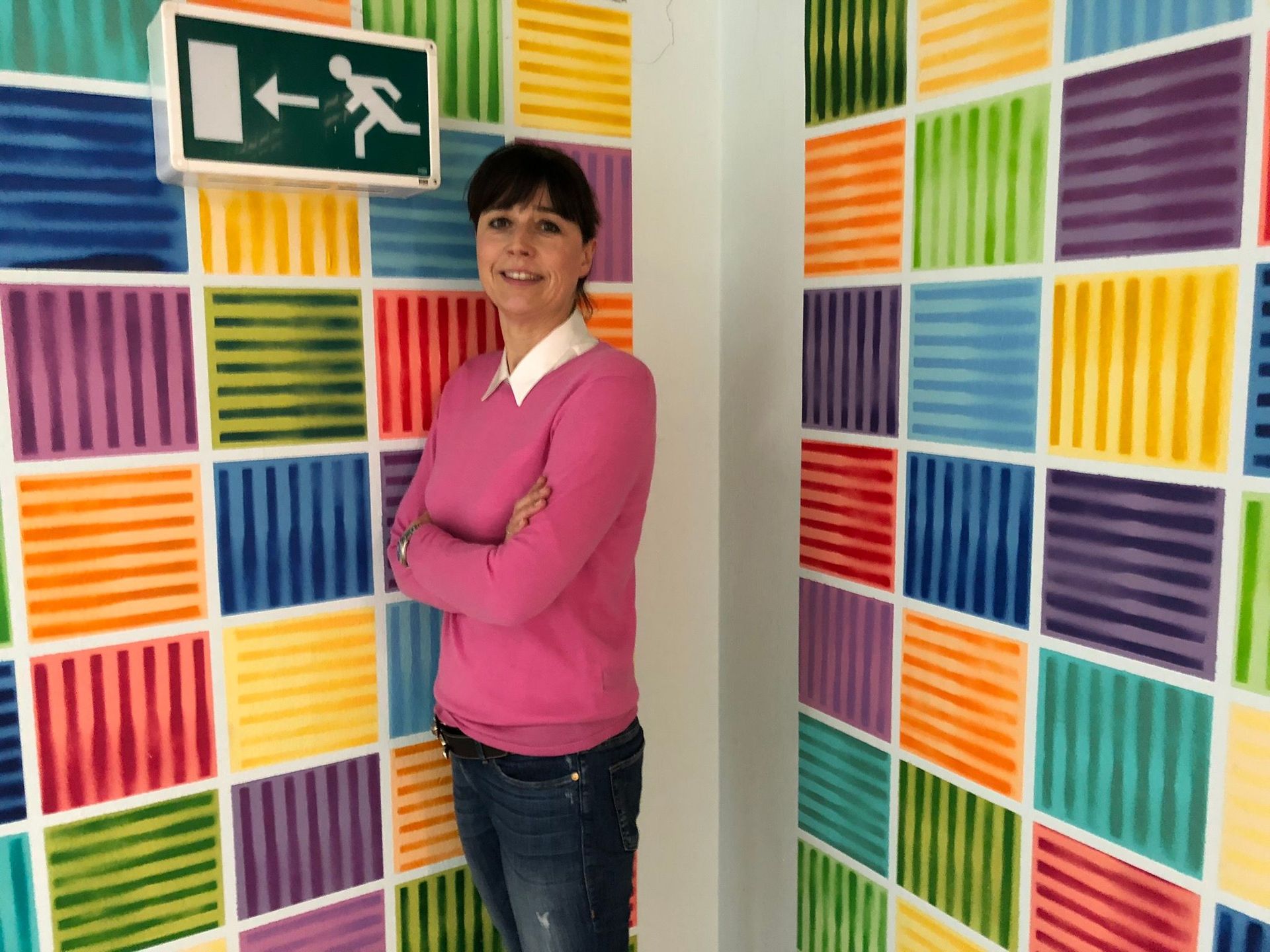 Claudia Marbach vor bunter Wand mit Notausgang-Zeichen.