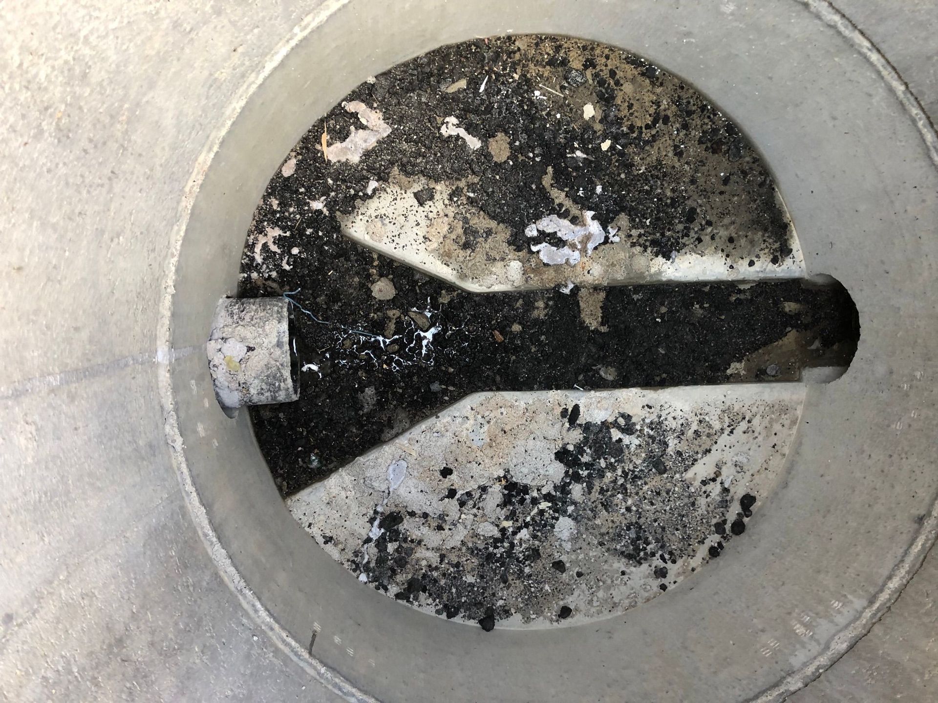 Übergabeschacht mit Asphaltresten in der Rohrsohle. Asphalt und Bauschutt im Schacht und in der Grundleitung - Rohrreinigung in Undeloh.