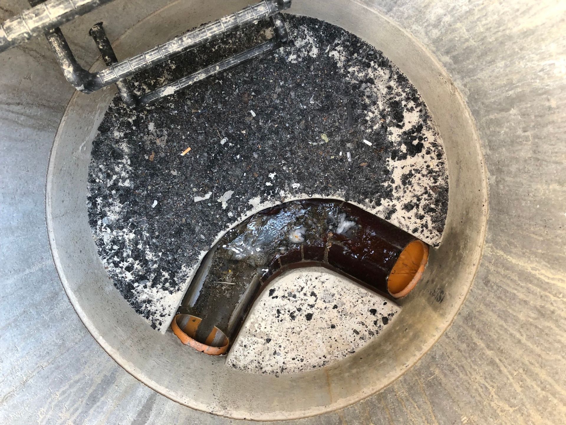 Asphaltreste im Übergabeschacht. Asphalt und Ablagerungen in einem Übergabeschacht. Rohrfrei Direkt - Rohrreinigung für Dittmern.