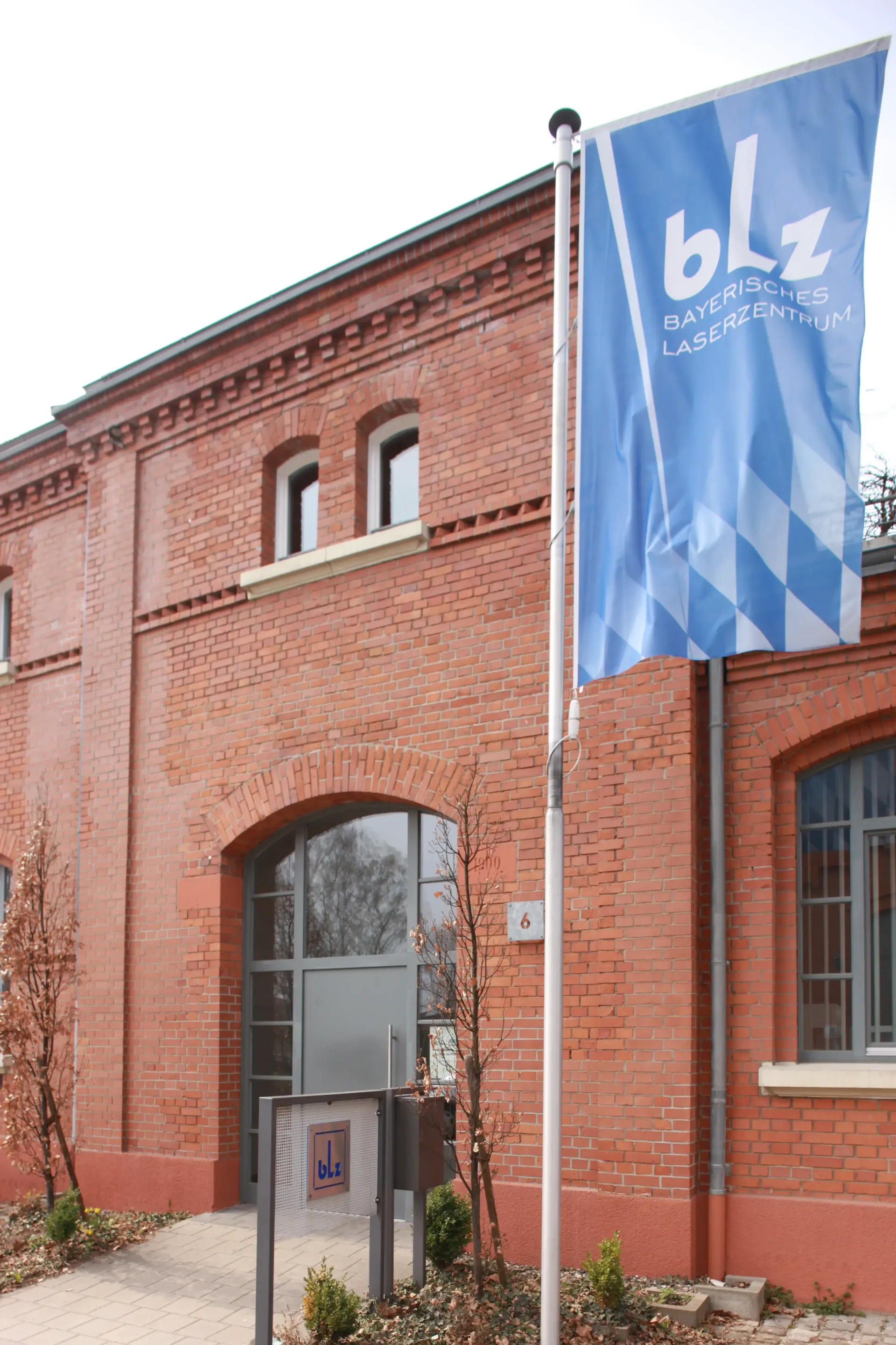 Außenansicht des Bayerischen Laserzentrums (blz) in Erlangen mit Flagge am historischen Backsteingebäude