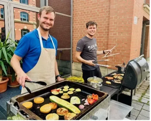 Zwei Geschäftsführer grillen Gemüse und Burger beim Sommerfest von blz und LPT.