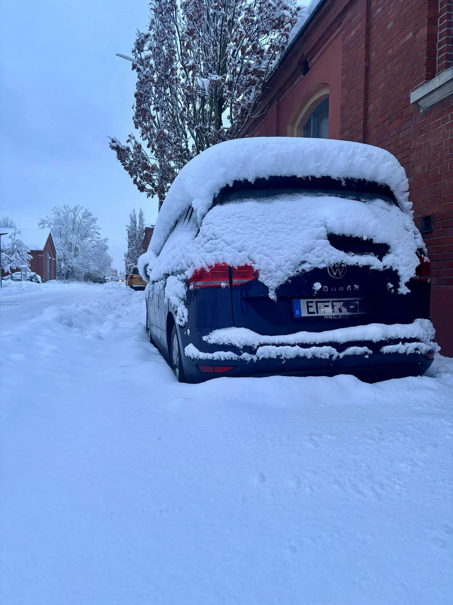 Verschneites Auto steht vor dem Gebäude des blz in Erlangen, die Straße und Bäume sind vollständig von Schnee bedeckt.