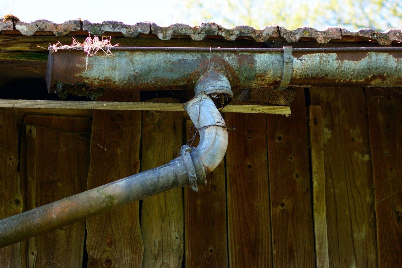 Eine Dachrinne an einem älteren Gebäude, bei der das Fallrohr nicht korrekt im Abflussloch sitzt – ein Hinweis auf Reparaturbedarf, um Wasserabflussprobleme zu vermeiden.