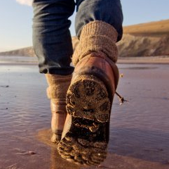 Person in walking boots walking on a beach Person in walking boots walking on a beach