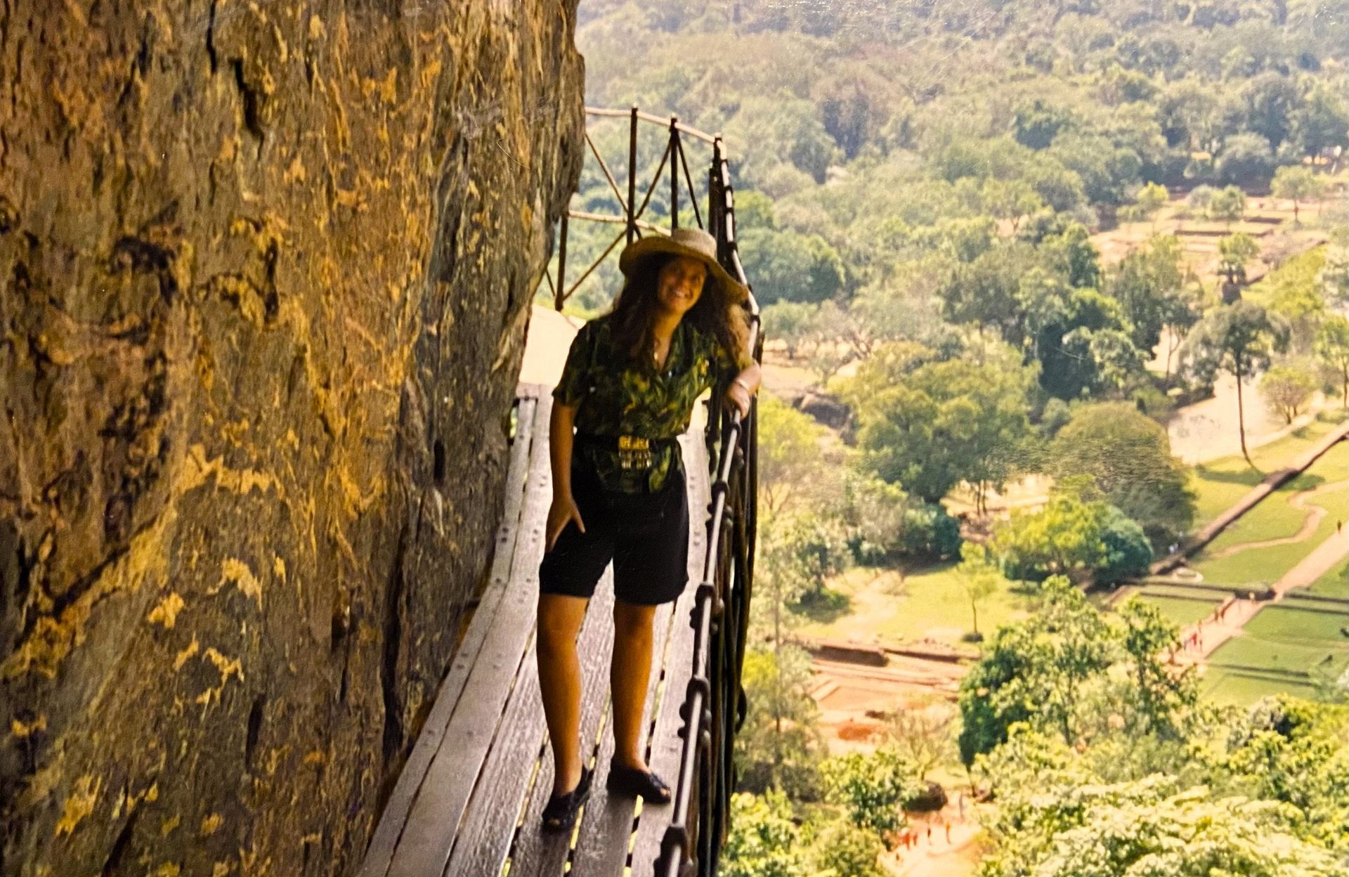 @Andrea Heidi Lagler - GEOlaViva Eine Frau mit Strohhut und grüner Bluse steht auf einem schmalen Steg entlang einer steilen Felswand. Im Hintergrund erstreckt sich eine weite, grüne Landschaft mit Bäumen und archäologischen Ruinen. Die Szene vermittelt das Gefühl von Abenteuer und Naturverbundenheit.
A woman in a straw hat and green blouse stands on a narrow footbridge along a steep rock face. In the background is a vast, green landscape with trees and archaeological ruins. The scene conveys a sense of adventure and closeness to nature.
@Andrea Heidi Lagler - GEOlaViva