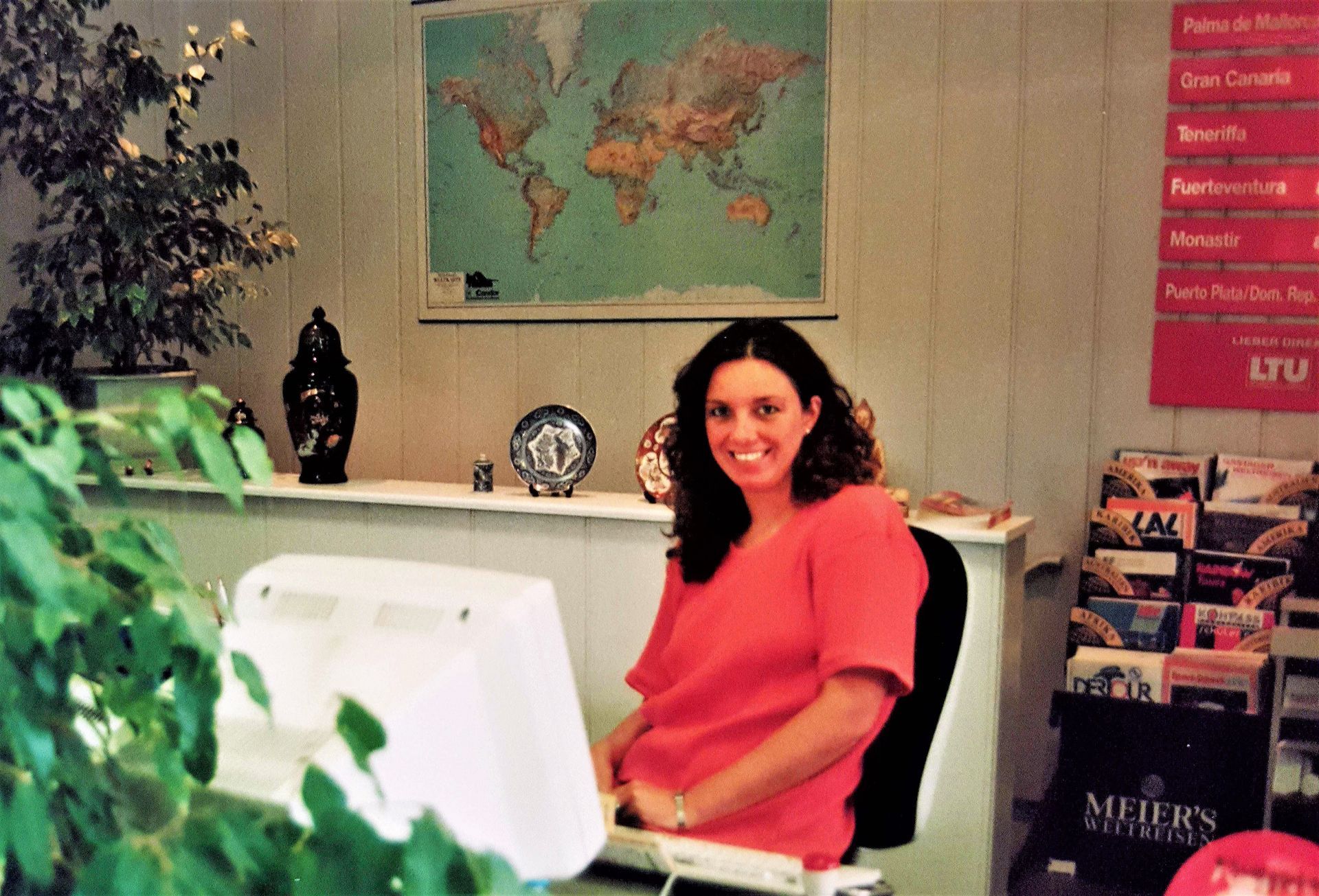 Eine Frau mit lockigem Haar sitzt lächelnd an einem Schreibtisch in einem Reisebüro. Sie trägt ein orangefarbenes Oberteil und wirkt herzlich und offen. Im Hintergrund sind eine Weltkarte, dekorative Vasen sowie Regale mit Reiseprospekten zu sehen. Eine ruhige und einladende Atmosphäre, die von der Liebe zum Reisen zeugt.
A woman with curly hair sits smiling at a desk in a travel agency. She is wearing a orange top and appears warm and open. A world map, decorative vases and shelves with travel brochures can be seen in the background. A calm and inviting atmosphere that testifies to a love of travel.
@Andrea Heidi Lagler - GEOlaViva