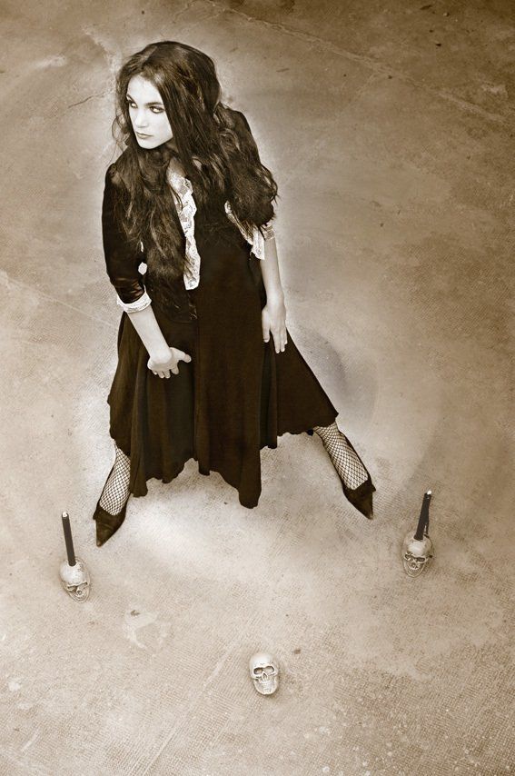 Thierry Aguiar : Photo sépia d'Albane en  gothique,debout en robe noire,  des bougies et un crâne posés à ses pieds.