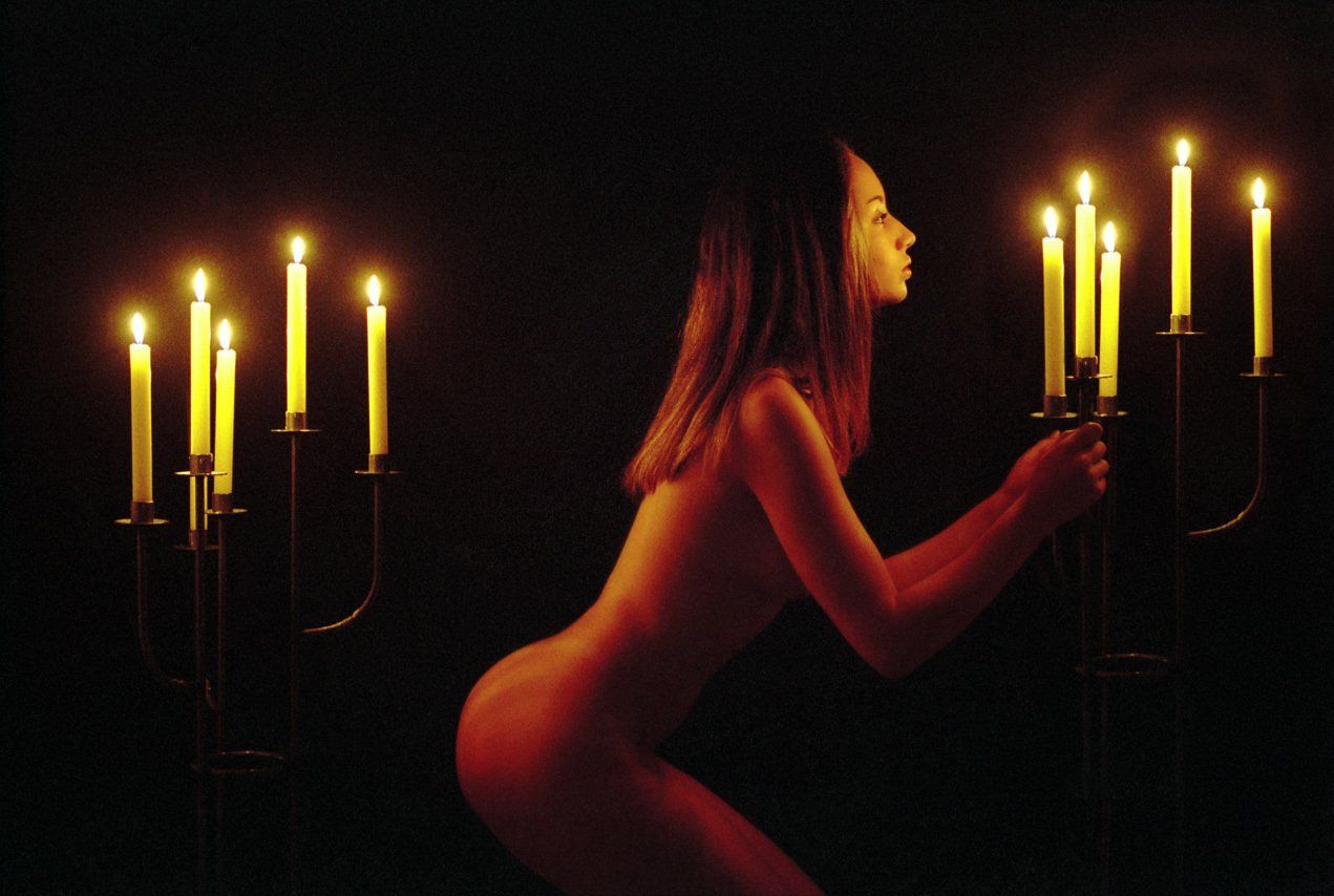 Thierry Aguiar : photo de Caroline nue éclairée par des bougies, debout de profil entre deux chandeliers sur pied.