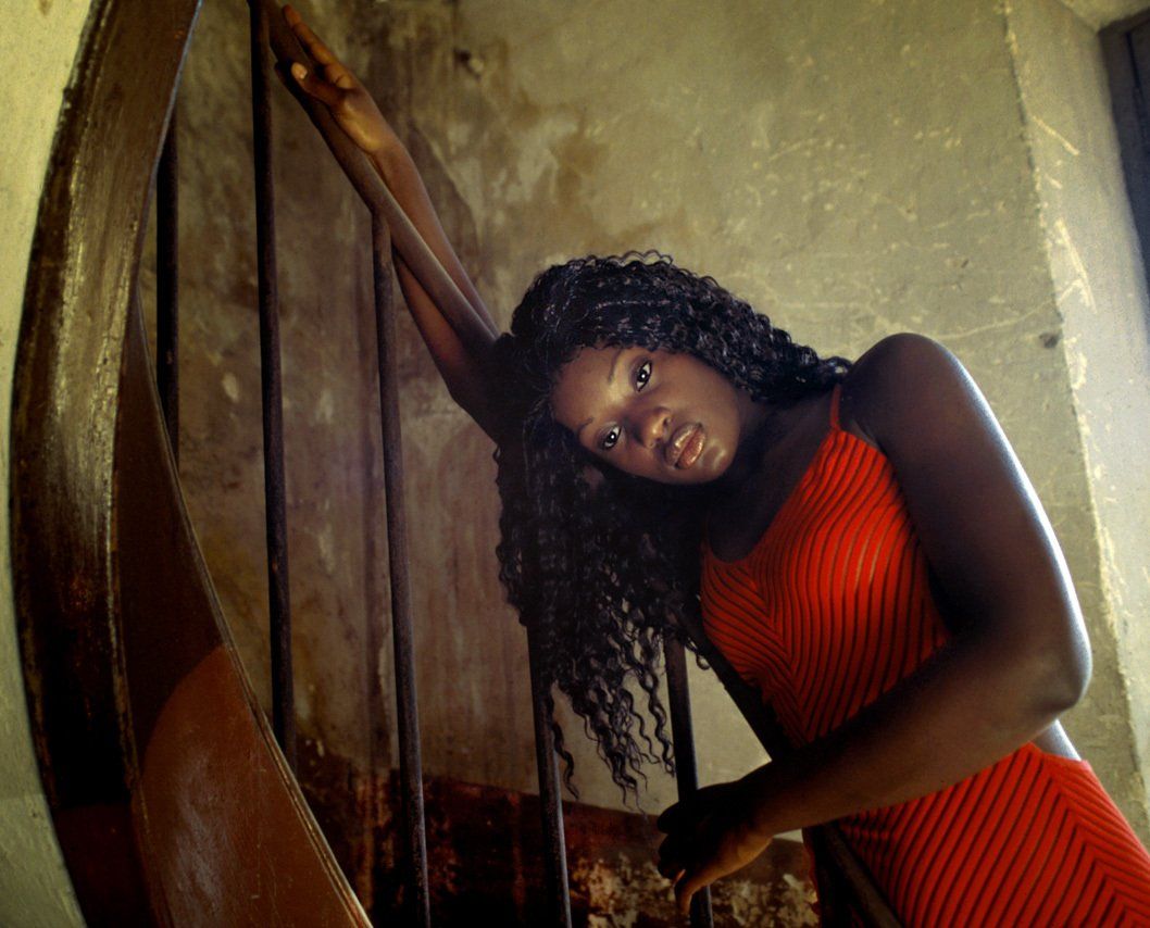 Thierry Aguiar : photo de Jessyca, jeune fille noire d'origine congolaise, , en lumière naturelle,  le côté droit allongé sur la rampe d'un escalier dans un bâtiment abandonné de Roure à Grasse.