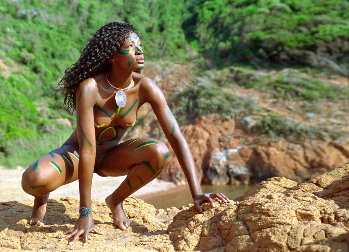 Thierry Aguiar : photo de Jessyca,  jeune fille noire d’origine congolaise, nue, accroupie sur des rochers regardant vers le ciel, au soleil levant dans les Adrets de l'Esterel. Le corps maquillé avec des traits de couleur, un collier tribal autour du cou, un bracelet fleur autour du poignet.