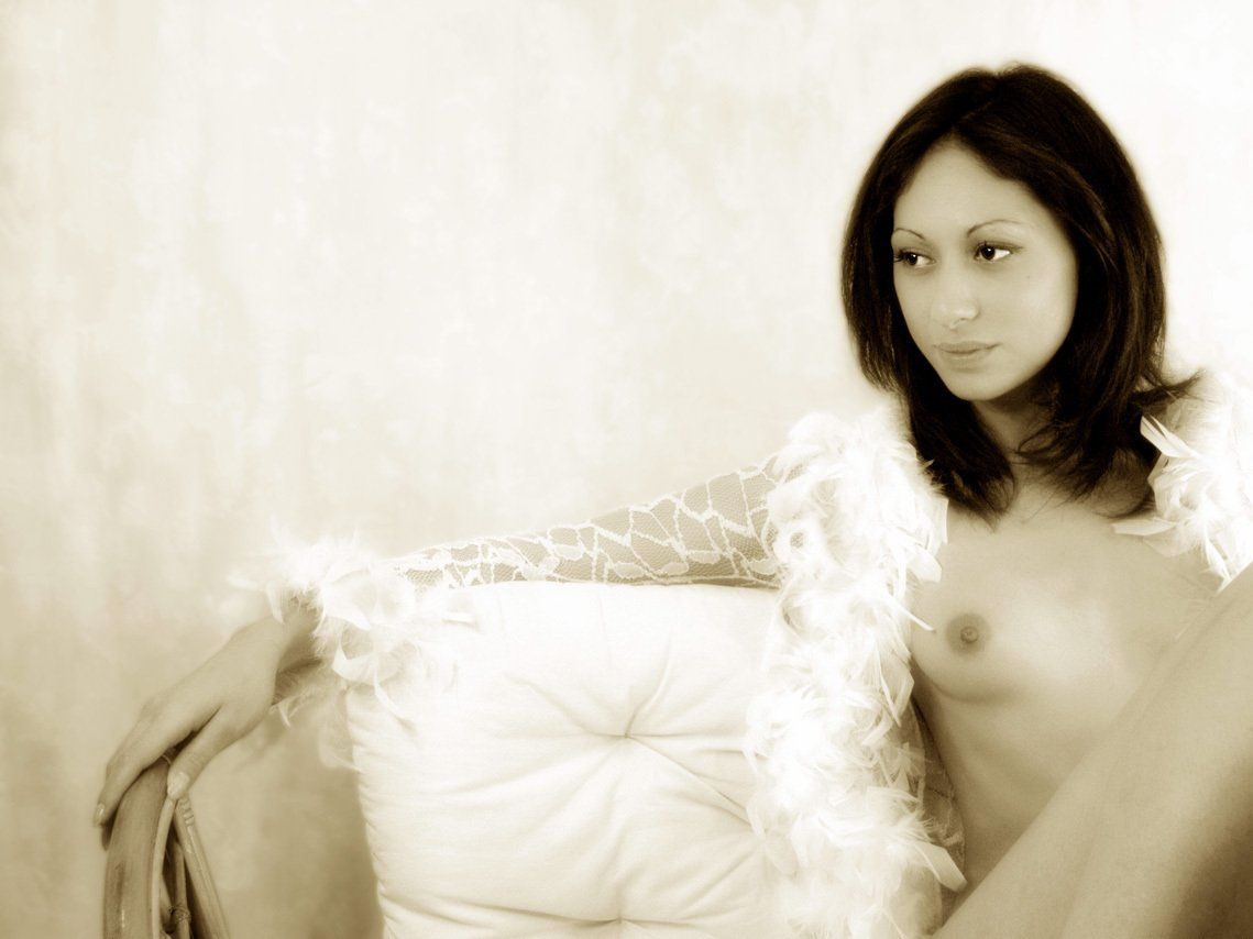 Thierry Aguiar : photo sépia de Juliana nue, assise sur un canapé en osier, l'air pensif, un chemisier en plume ouvert sur sa poitrine. Photo publiée dans Photofan.