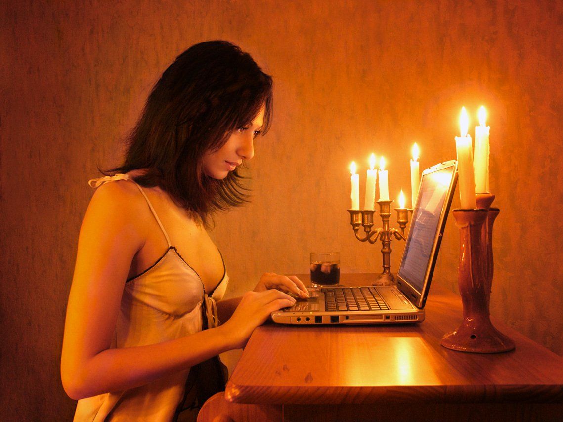 Thierry Aguiar : Juliana en nuisette en train d'écrire à l’ordinateur sur un comptoir de bar, éclairée par des bougies.