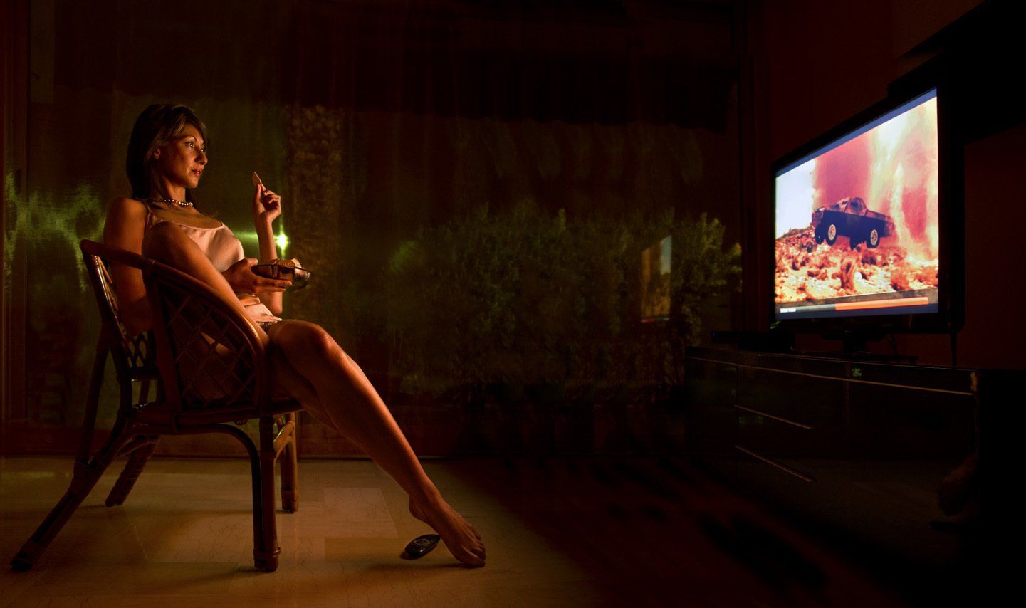 Thierry Aguiar : photo  de Juliana  en nuisette de soie sur un fauteuil en osier,   mangeant des gâteaux en regardant la télé