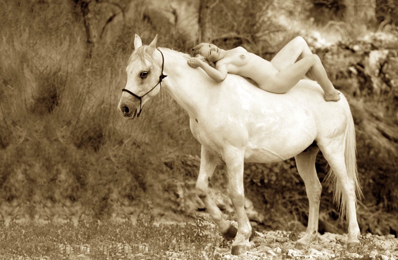 Thierry Aguiar : photo sépia en extérieur dans une forêt de Malika, jeune fille blonde, nue allongée sur le dos sur un cheval blanc.