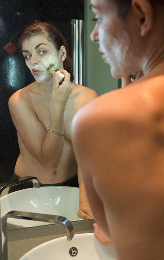 Manéa jeune fille aux yeux verts, nue devant un miroir de salle de bains, se passant de la mousse à raser sur le visage.