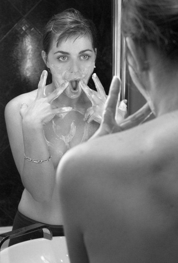 Thierry Aguiar : photo noir et blanc de Manéa, jeune fille aux yeux verts, nue devant le miroir de la salle de bains, de la mousse à raser sur le torse, faisant la grimace.