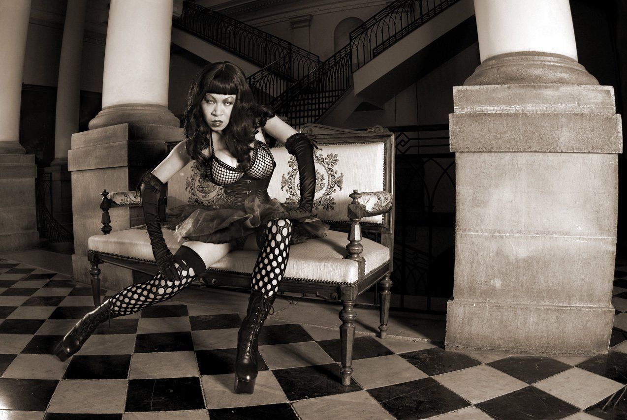 Photo sépia de Masako d'origine japonaise,  sur un canapé dans un bâtiment du 19ème siècle, portant bas résilles et bustier