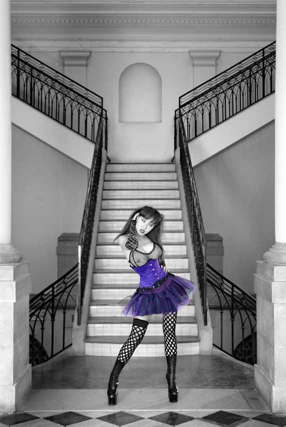 Masako, d'origine japonaise, debout devant l'escalier d'un bâtiment du 19ème siècle, portant  bas résilles et bustier violet