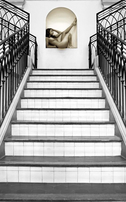 Thierry Aguiar : photo d'Inditalia nue, assise de profil dans une niche d'un mur de l'ancien Palais de Justice à Grasse, bâtiment du 19ème siècle, 1840. Photo prise dans la perspective de l'escalier.