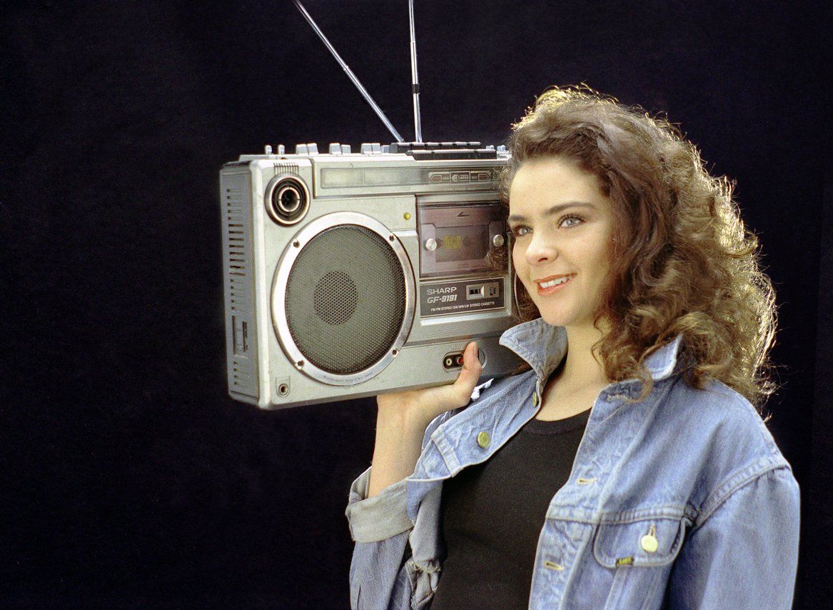 Thierry Aguiar : Photo de Sophie souriante, portant une veste en jean, un radio k7 des 80's sur l'épaule.