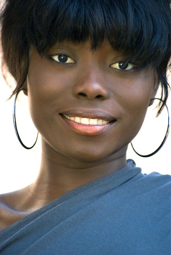 Thierry Aguiar : Portrait de face en lumière naturelle et en extérieur de Vanessa, jeune fille noire d'origine congolaise, souriante, portant des boucles d'oreilles créoles.