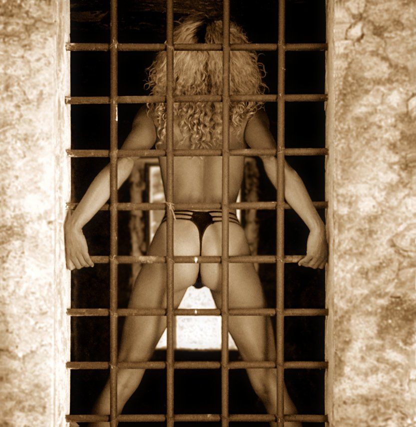Thierry Aguiar : photo de Virginie, jeune fille métisse d’origine camerounaise, nue, portant un string noir, debout de dos derrière les barreaux de la fenêtre d’un bâtiment abandonné dans le Var.