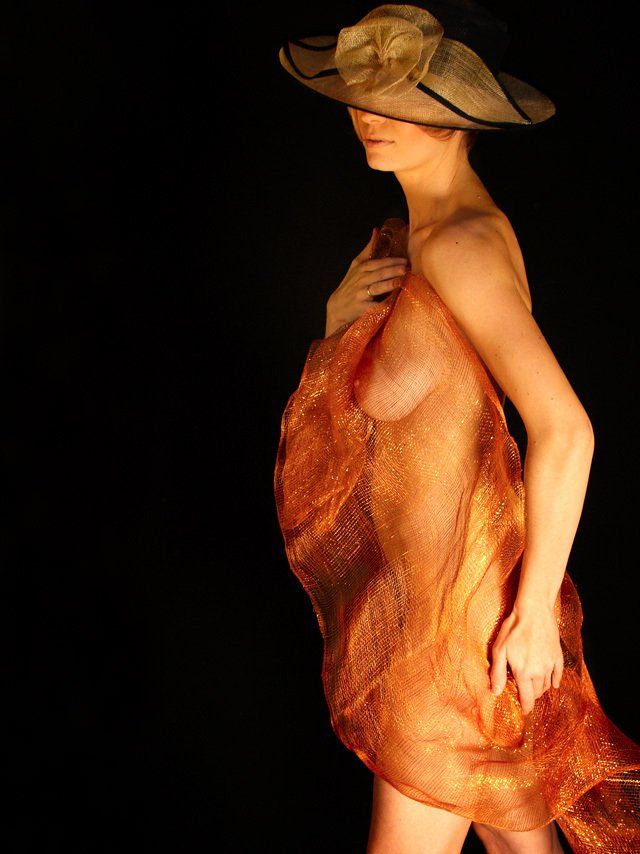 Thierry Aguiar : photo de Valérie nue, debout de profil, portant un chapeau de tulle doré, et un tulle doré autour du corps.