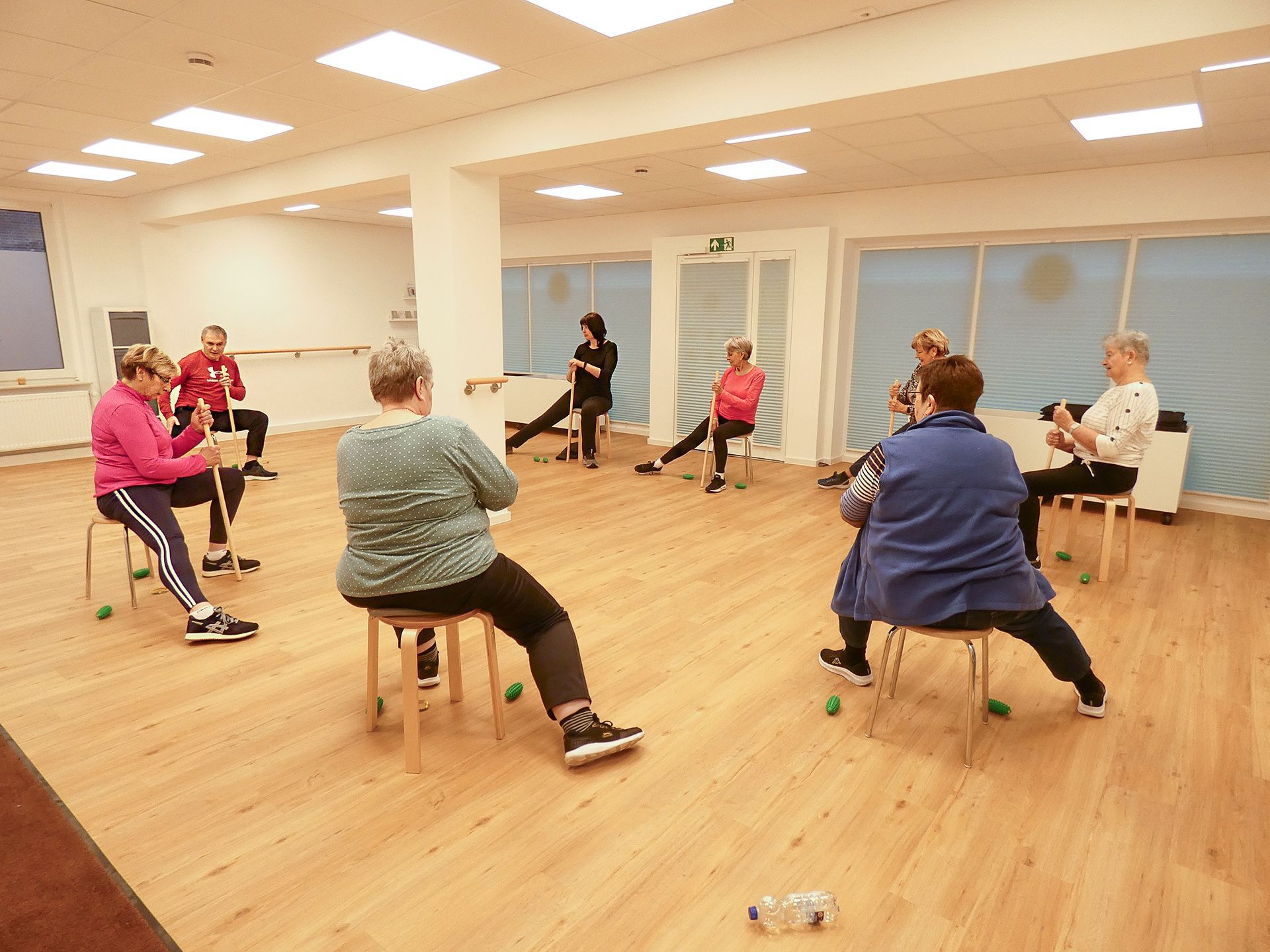 Hockergymnastik im Seminar- und Bewegungsraum der Reha-Sportgruppe Wardenburg. Die Teilnehmer machen eine Übung mit dem Stab.