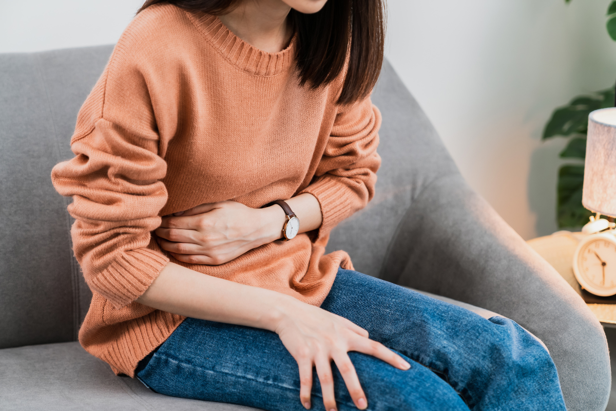 woman in orange sweater holds hand over stomach to signify stomach ache