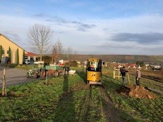 Ein Minibagger und ein Traktor auf dem Feld. Daneben Landarbeiter neben einem kleinen Erdhügel. Ein Minibagger und ein Traktor auf dem Feld. Daneben Landarbeiter neben einem kleinen Erdhügel.