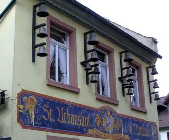 Auf dem Bild sieht man den Sankt Urban Hof drei Fenster im ersten Stock jeweils umrahmt von Winkeln die Glocken tragen, die beiden äußeren Winkel tragen jeweils drei Glocken die beiden inneren Winkel jeweils fünf.