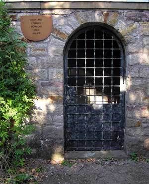 Natursteinwand mit vergitterten Eingang und Schild Natursteinwand mit vergitterten Eingang und Schild