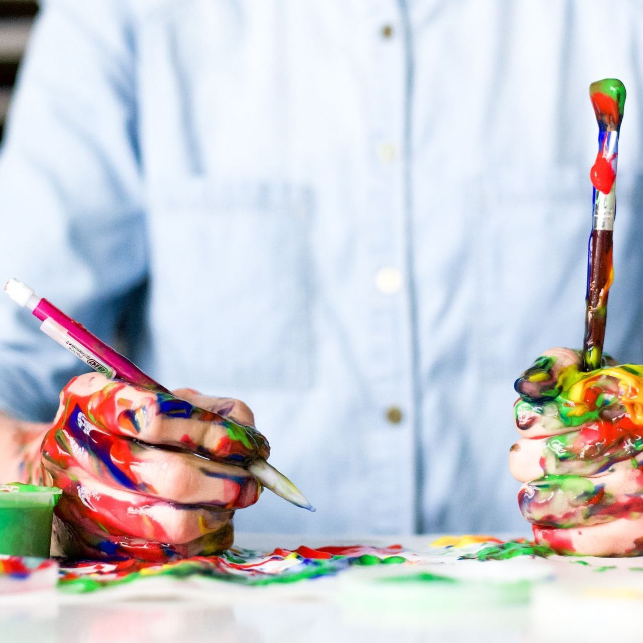 Ein Mann im Helmd mit farbverschmierten Händen hält jeweils einen Stift und einen Pinsel in der Hand