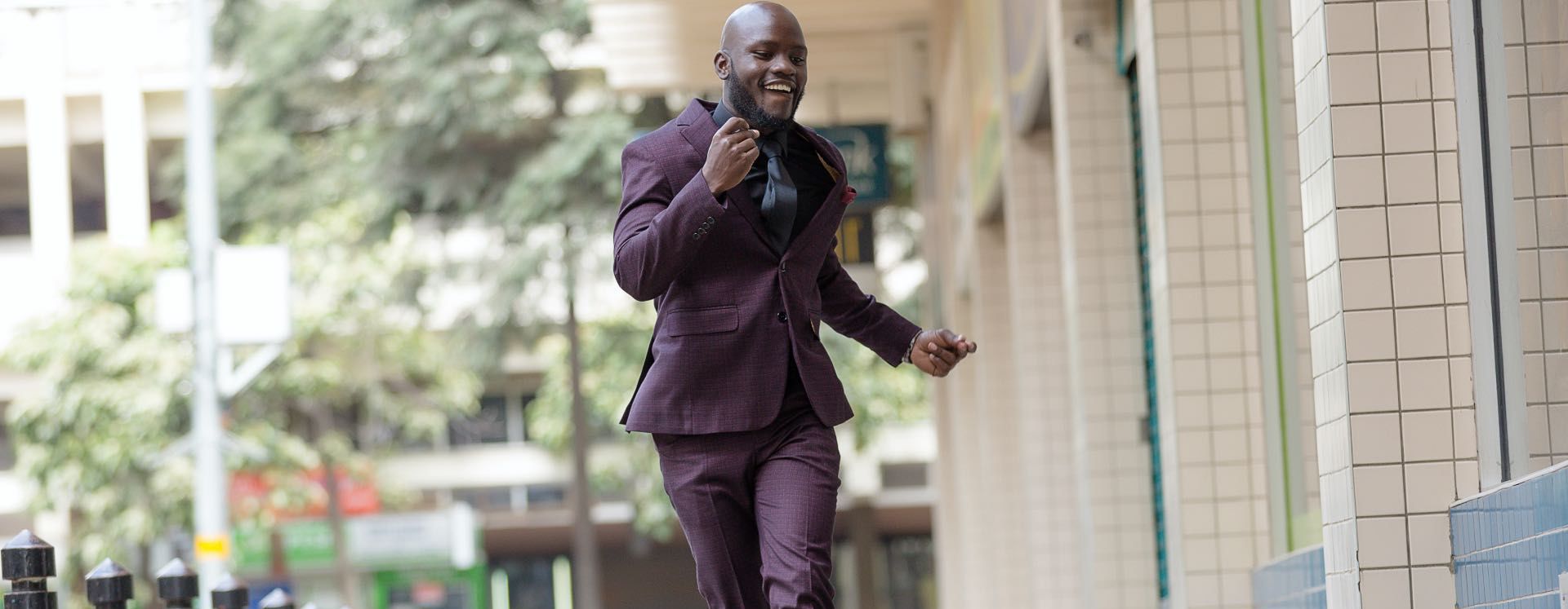 Glücklicher, tanzender Mann in violettem Anzug bei Tageslicht auf dem Gehweg