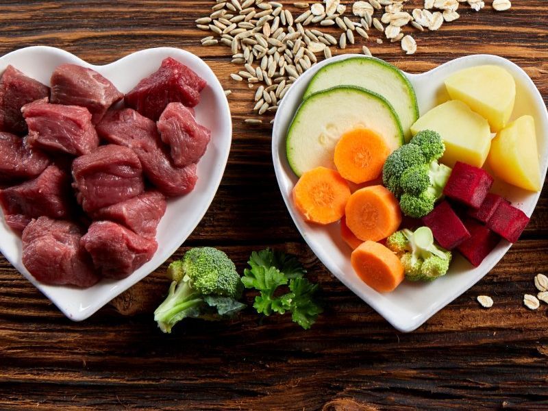 Vier herzförmige Näpfe, einer gefüllt mit rohem Rind, einer mit Gemüse in Stückchen, einer mit Lachs und Garnelen und einer mit roher Leber und Reis