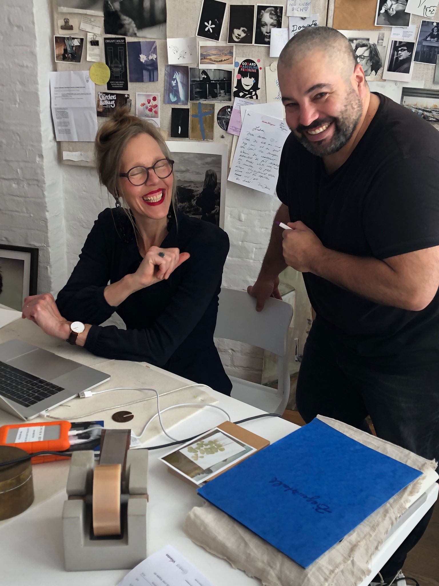 Leiter des Kurses für Kameraschauspiel, Samuel Núñez, lachend an einem Schreibtisch mit der Fotografin Donata Wenders.