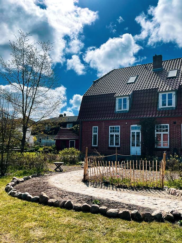 Ein liebevoll gestalteter Bauerngarten mit gepflasterten Wegen und einem Staketenzaun auf einem Ferienhof auf Fehmarn