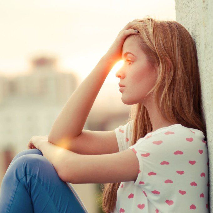 Photo of a young woman with blond hair sitting down against an exterior wall.
